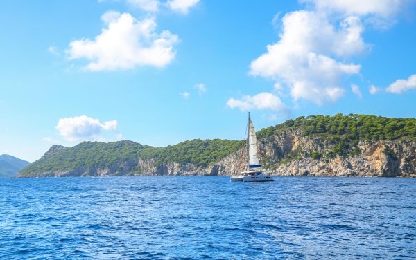 A serene view of a sailboat navigating the blue waters near rocky cliffs and green landscapes in Dubrovnik. A serene view of a sailboat navigating the blue waters near rocky cliffs and green landscapes in Dubrovnik.