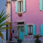 Vibrant pink house with teal shutters in Fažana, showcasing Mediterranean charm.