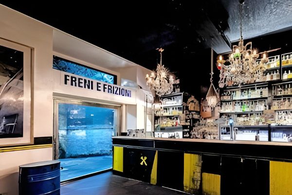 Freni e Frizioni bar in Trastevere Rome set inside a converted mechanics workshop with black and bright yellow decor. Mechanical memorabilia mixes with crystal chandeliers and a wall of spirits creating a unique aperitivo spot for cocktails and lively evenings.