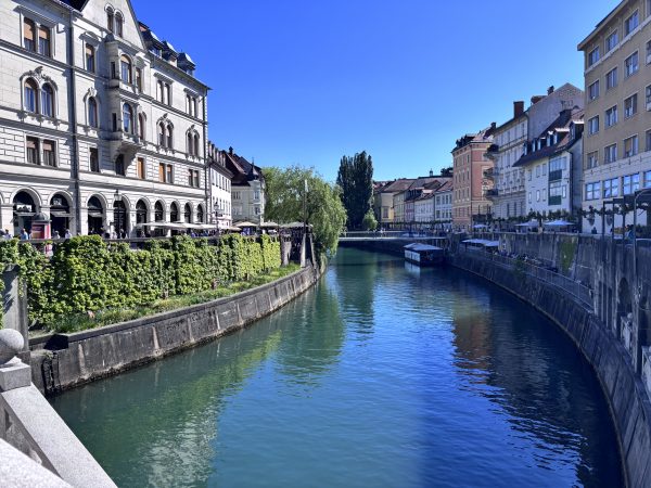 Beautiful spring day on the banks of the river Ljubljanica . Vivid blue sky, reflecting on emerald green water. the building on the banks are ornate with arches and balconies.