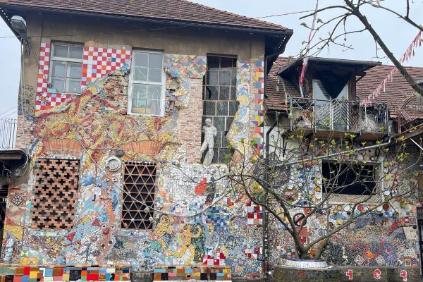 Building at Metelkova in Ljubljana covered in bright ceramic artwork depicting Roman gods whimsical figures and playful objects. The colorful facade reflects the creative alternative spirit of the autonomous cultural district known for its street art and underground culture.