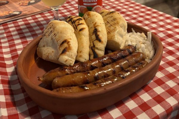 Traditional Slovenian Meal of Beef Sausages, Traditional Bread and Onion. Served on a terracotta plate on a red and white gingham table cloth.