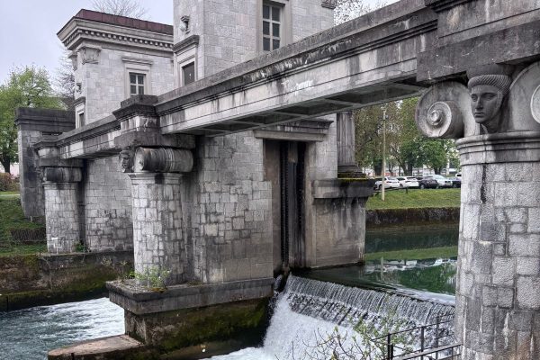 Beautiful Sluice Gate Bridge is on the river Ljubljanica. three stone-covered towers spanning the water, heavily inspired by ancient Egyptian temple architecture. The towers feature tall, classical columns, vases with carved dragon heads, and low arches that support an integrated footbridge. Primarily built to regulate the water level of the Ljubljanica River and prevent flooding in the city center, it creates a hydraulic head with a to meter difference across the gate.