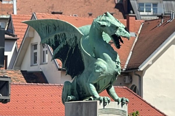 Ferocious copper dragon statue perched on Dragon Bridge in Ljubljana with wings spread and detailed scales visible against the city skyline. The early 20th century bridge is one of Ljubljana’s most recognizable landmarks and an important example of Art Nouveau engineering.