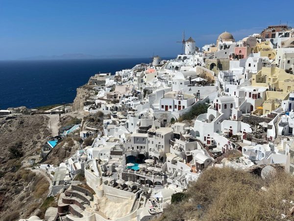 Aerial view of Santorini, Greece, showcasing whitewashed buildings with domes and balconies, a windmill, and the deep blue sea under a clear sky.