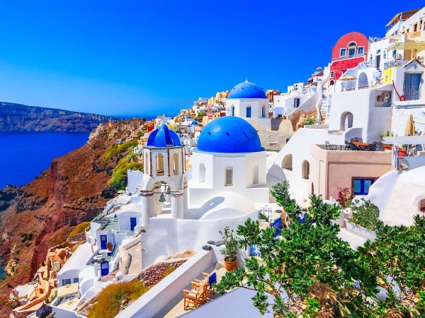 Santorini's iconic white buildings with blue domes overlook the deep blue sea under a clear sky. Vibrant, picturesque, and serene coastal scenery.