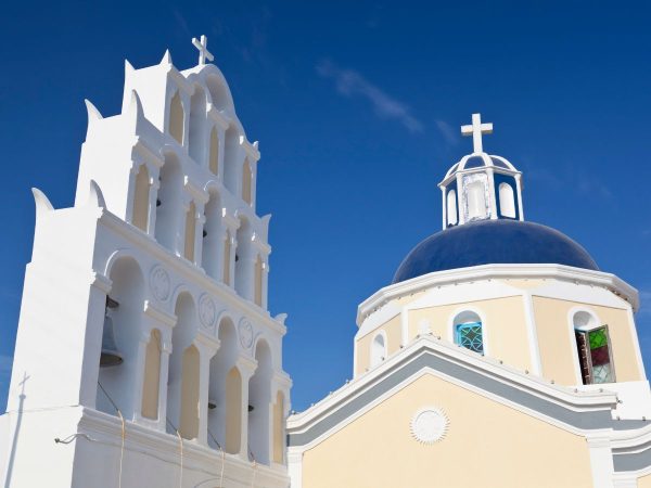 White church with a bell tower and blue dome under a clear sky. The architecture is classic, conveying serenity and Mediterranean charm.