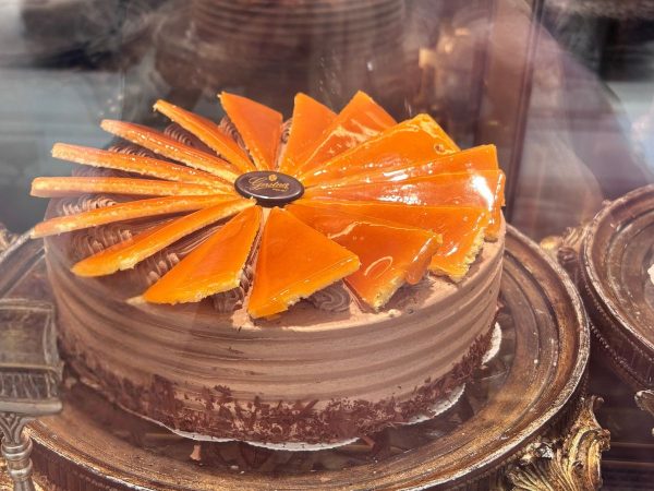 A rich chocolate cake with glossy orange glaze slices arranged on top, displayed on a decorative tray, exudes an indulgent, luxurious appeal.