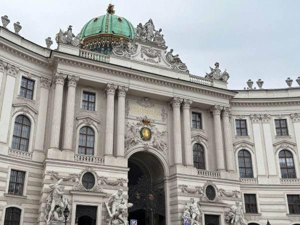 Ornate Baroque building facade featuring a large archway, statues, and a green dome. The intricate details convey a sense of grandeur and history.