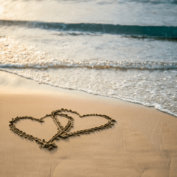 2 heart overlapping draw into the sand at the beach. waves lapping up in the background.