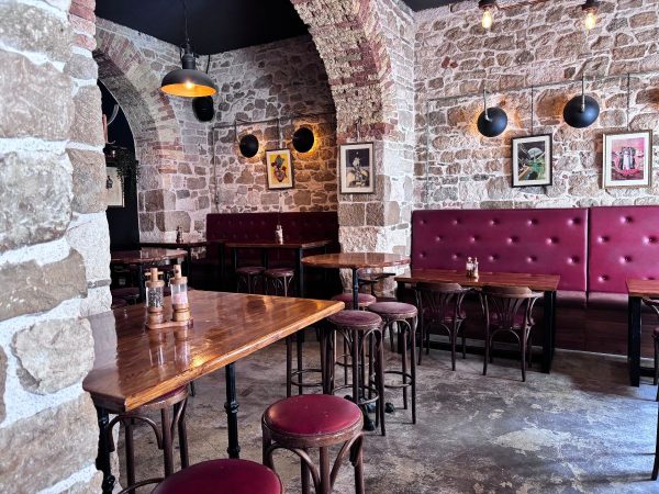 The Daltonist (1) The interior of a cozy stone-walled bar with arched brick doorways, dark wood tables, burgundy leather booth seating and stools, framed artwork on the walls, and warm pendant lighting. Super bar in Split, Croatia